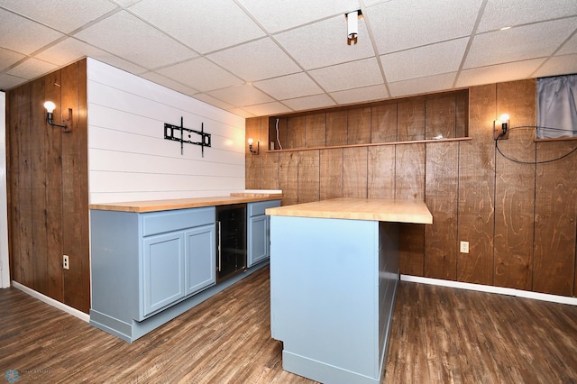 bar featuring beverage cooler, dark wood-type flooring, wood counters, a paneled ceiling, and wooden walls