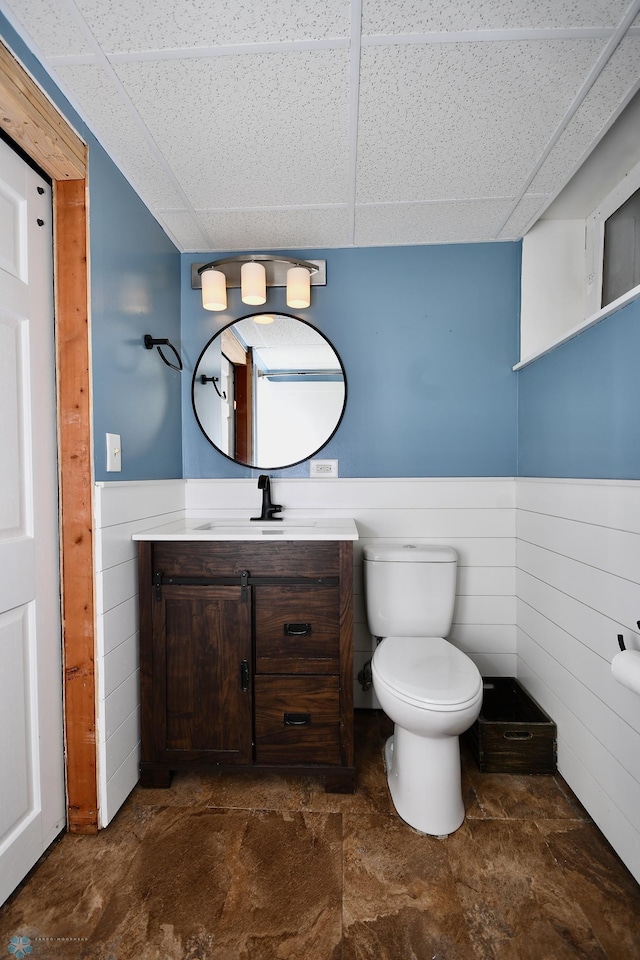 bathroom with a paneled ceiling, vanity, wood walls, and toilet