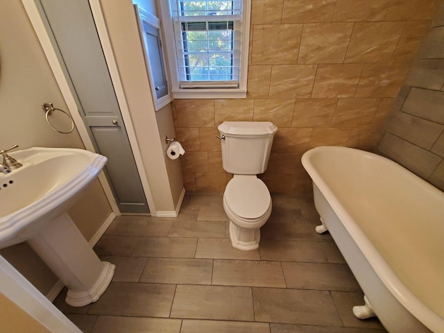 bathroom featuring tile patterned floors, a washtub, tile walls, and toilet