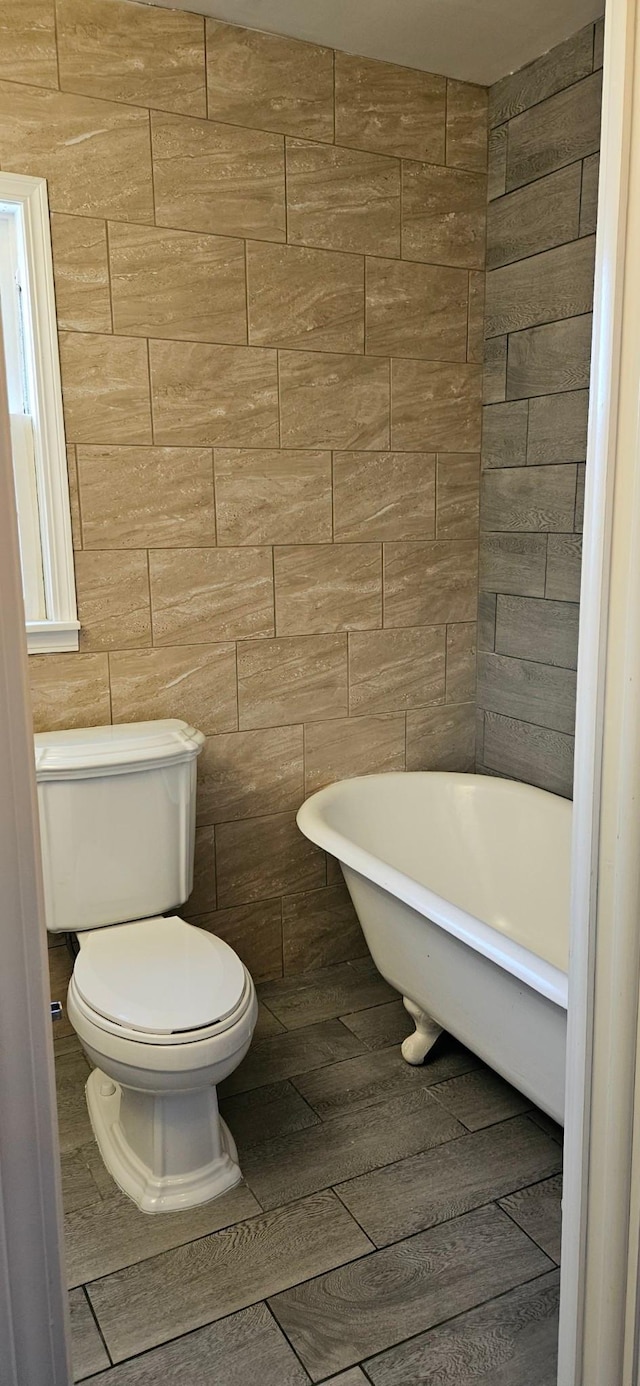 bathroom with hardwood / wood-style flooring, toilet, tile walls, and a bathing tub