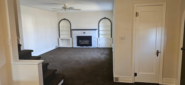 unfurnished living room with a brick fireplace, ceiling fan, and dark colored carpet