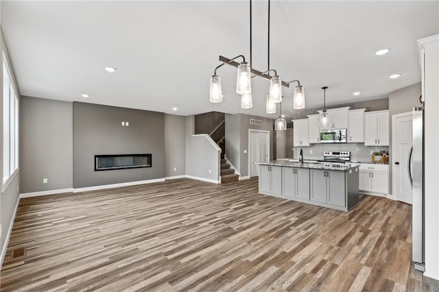 kitchen featuring white cabinets, hanging light fixtures, light hardwood / wood-style flooring, an island with sink, and stainless steel appliances