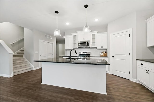 kitchen with stainless steel appliances, a kitchen island with sink, sink, white cabinets, and dark hardwood / wood-style floors