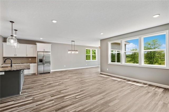 kitchen with white cabinetry, stainless steel built in refrigerator, hanging light fixtures, and dark stone counters