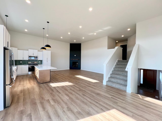 kitchen with light wood-style flooring, white cabinets, a kitchen island, appliances with stainless steel finishes, and open floor plan