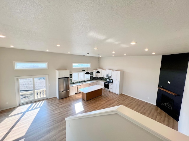 kitchen with a textured ceiling, white cabinets, stainless steel appliances, open floor plan, and light wood finished floors