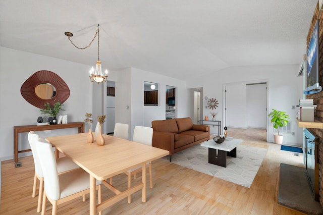 dining area featuring a notable chandelier, vaulted ceiling, and light wood-type flooring