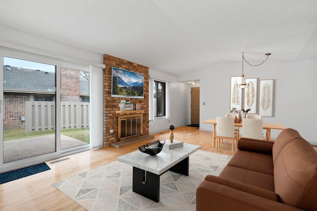 living room featuring a chandelier, light wood-type flooring, a brick fireplace, and lofted ceiling