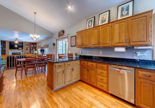 kitchen featuring a fireplace, dark stone countertops, hanging light fixtures, stainless steel dishwasher, and kitchen peninsula