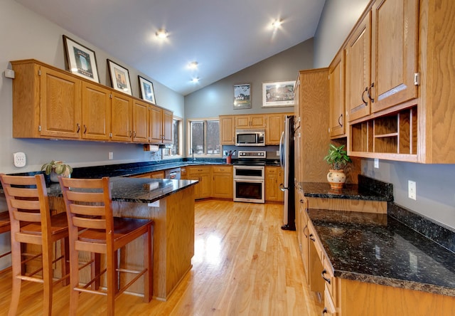 kitchen with a kitchen bar, light hardwood / wood-style flooring, dark stone countertops, appliances with stainless steel finishes, and kitchen peninsula