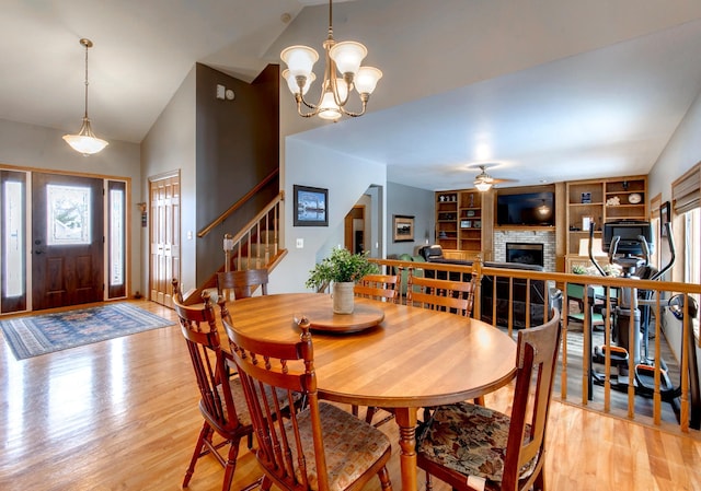 dining space featuring ceiling fan with notable chandelier, vaulted ceiling, light hardwood / wood-style floors, and built in shelves