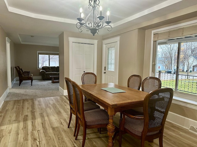 dining space featuring light wood-type flooring, a tray ceiling, and a notable chandelier