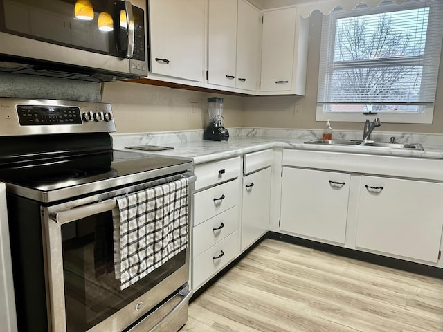 kitchen with appliances with stainless steel finishes, light hardwood / wood-style floors, white cabinetry, and sink