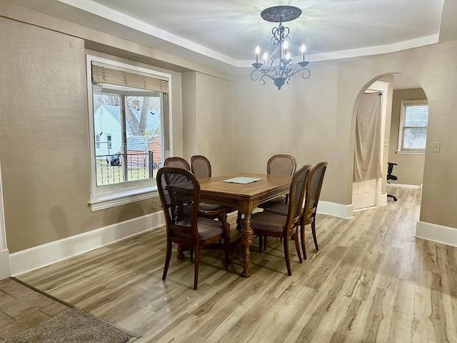 dining space featuring a raised ceiling, a chandelier, and light wood-type flooring