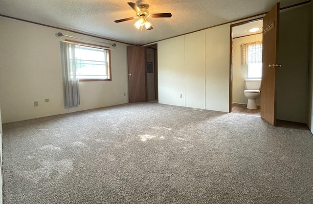 unfurnished bedroom featuring carpet flooring, ensuite bath, ceiling fan, and a textured ceiling