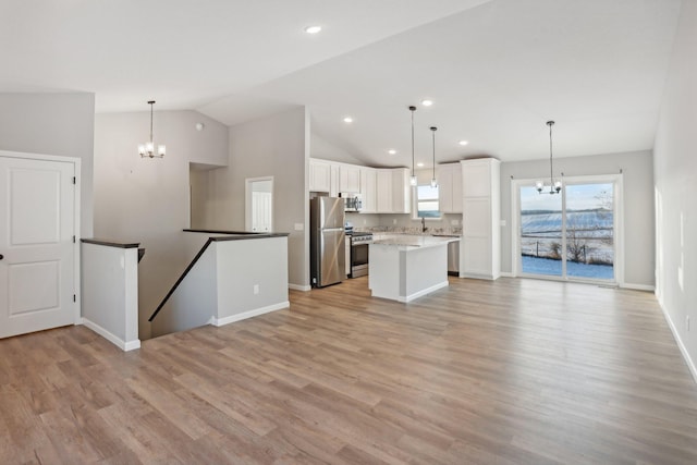 kitchen featuring hanging light fixtures, vaulted ceiling, a kitchen island, white cabinetry, and stainless steel appliances