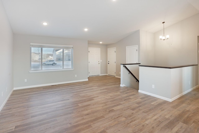 unfurnished room featuring a notable chandelier, light wood-type flooring, and vaulted ceiling