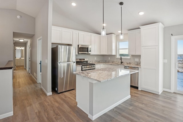 kitchen featuring white cabinets, appliances with stainless steel finishes, decorative light fixtures, a kitchen island, and light wood-type flooring