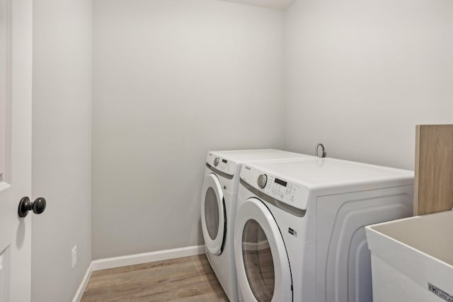 clothes washing area with light hardwood / wood-style flooring, washer and dryer, and sink