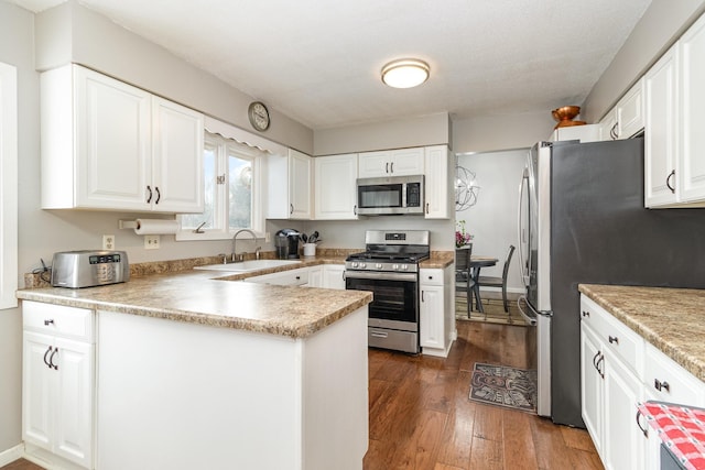 kitchen with stainless steel appliances, a peninsula, dark wood-style flooring, a sink, and white cabinetry