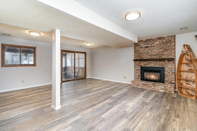 unfurnished living room featuring a wealth of natural light, visible vents, a brick fireplace, wood finished floors, and baseboards