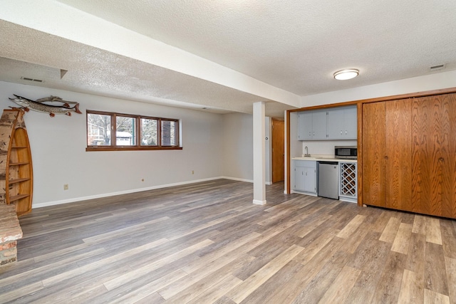 unfurnished living room featuring baseboards, a textured ceiling, visible vents, and light wood-style floors