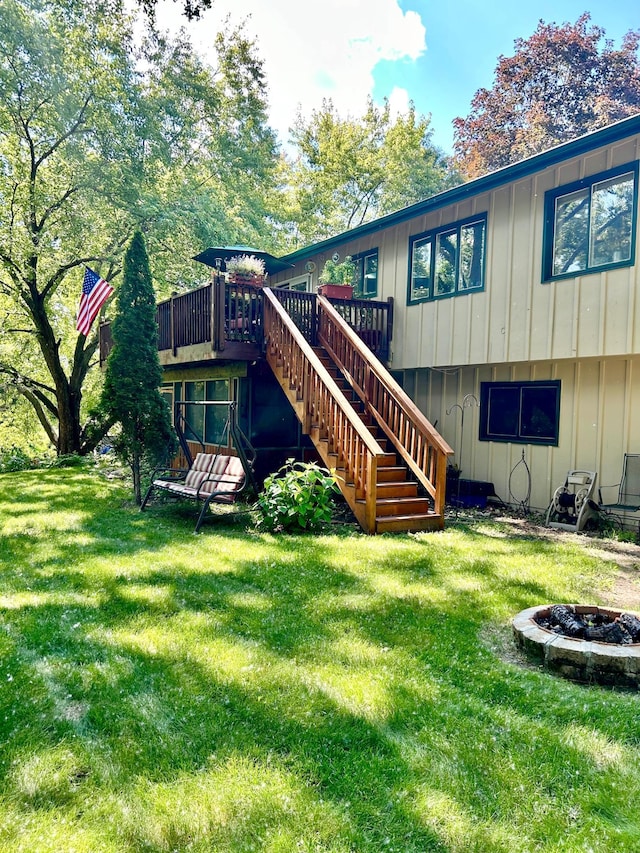 back of house featuring a deck, an outdoor fire pit, stairway, a lawn, and board and batten siding