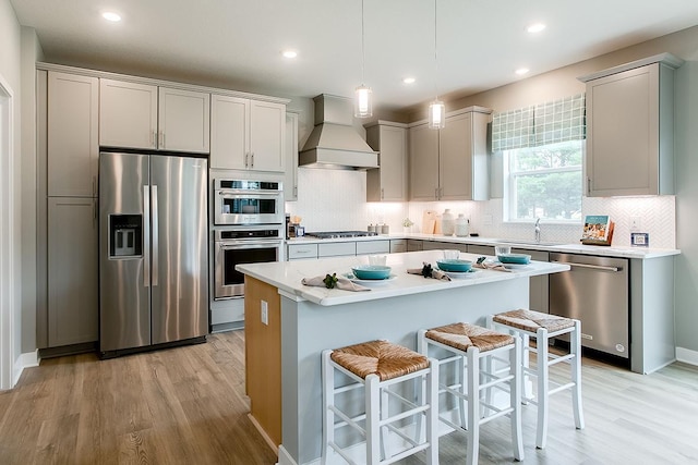 kitchen featuring light wood-type flooring, tasteful backsplash, custom exhaust hood, stainless steel appliances, and a center island