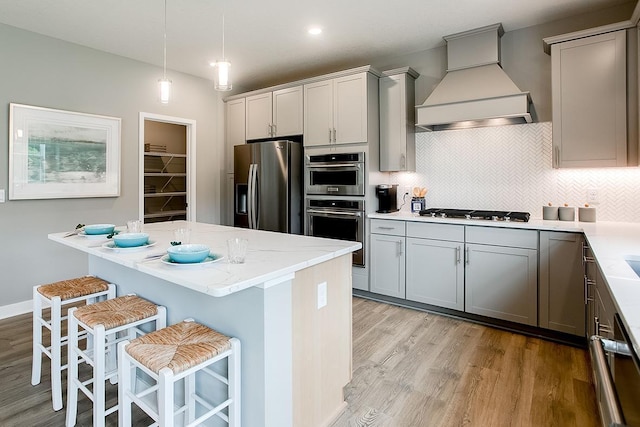 kitchen featuring decorative light fixtures, a kitchen bar, premium range hood, and appliances with stainless steel finishes