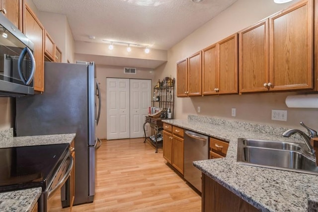 kitchen with sink, light stone counters, built in desk, light wood-type flooring, and appliances with stainless steel finishes