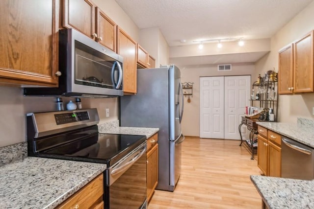 kitchen featuring track lighting, light stone countertops, a textured ceiling, and appliances with stainless steel finishes