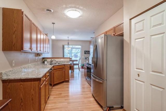 kitchen featuring sink, appliances with stainless steel finishes, hanging light fixtures, a textured ceiling, and kitchen peninsula