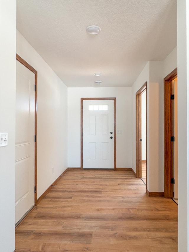 foyer with light wood-style floors, a textured ceiling, and baseboards