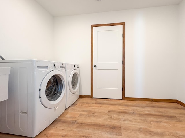 washroom featuring laundry area, baseboards, separate washer and dryer, and light wood-style floors