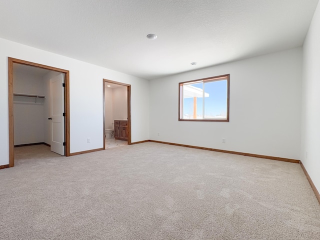 unfurnished bedroom featuring a walk in closet, light colored carpet, and baseboards