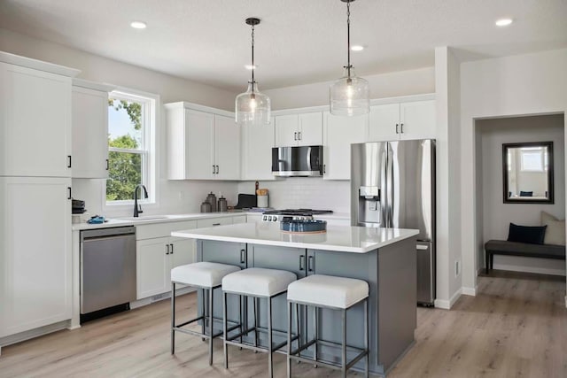 kitchen with white cabinets, appliances with stainless steel finishes, light hardwood / wood-style floors, and a kitchen island