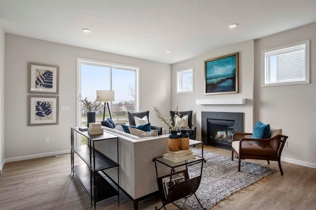 living room featuring recessed lighting, baseboards, a glass covered fireplace, and light wood-type flooring