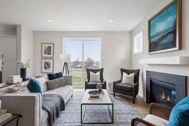 living area with recessed lighting, a glass covered fireplace, and wood finished floors