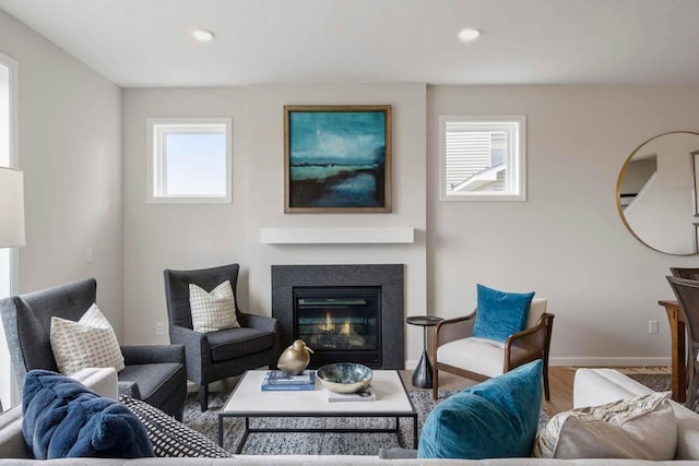 living area featuring a glass covered fireplace, baseboards, recessed lighting, and wood finished floors