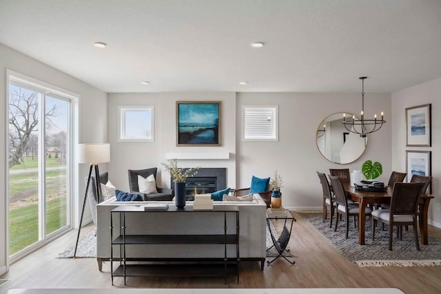 living area featuring an inviting chandelier, baseboards, a glass covered fireplace, and wood finished floors
