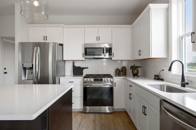 kitchen with tasteful backsplash, a sink, light countertops, stainless steel appliances, and white cabinetry