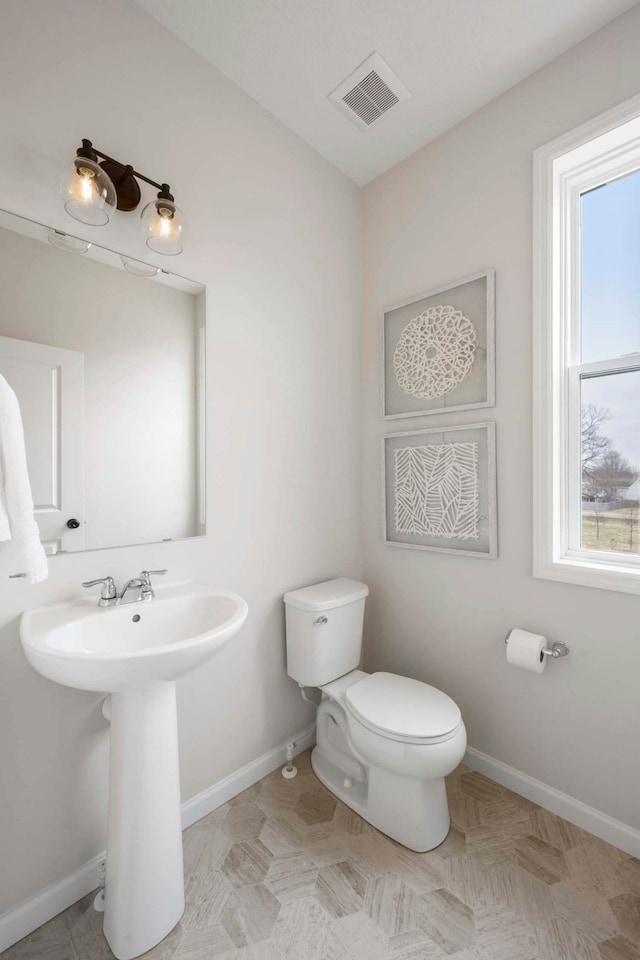 half bath featuring toilet, baseboards, visible vents, and plenty of natural light