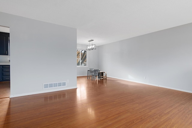 empty room with hardwood / wood-style flooring, a notable chandelier, and a textured ceiling