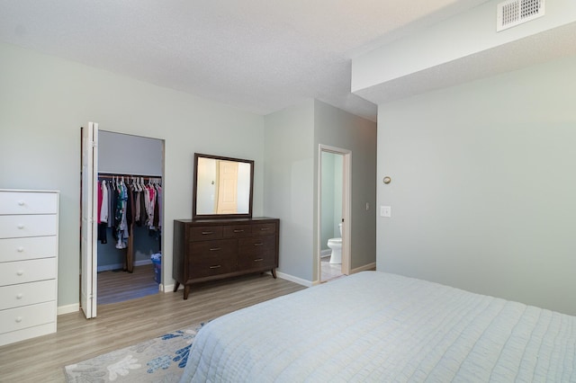 bedroom featuring connected bathroom, light hardwood / wood-style flooring, a textured ceiling, a walk in closet, and a closet