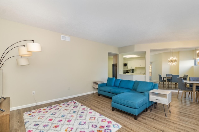 living room featuring a notable chandelier, baseboards, visible vents, and light wood finished floors