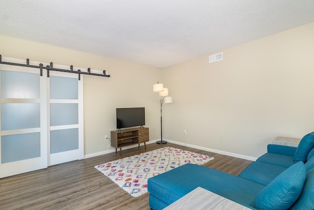 living room with visible vents, baseboards, a barn door, wood finished floors, and a textured ceiling