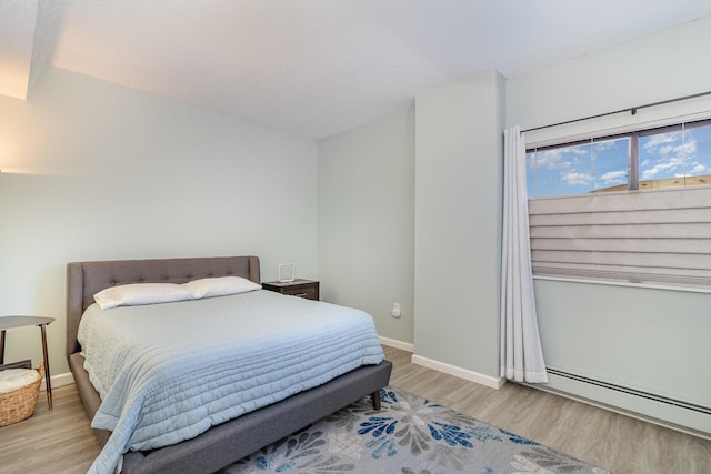 bedroom with a baseboard heating unit, baseboards, and wood finished floors