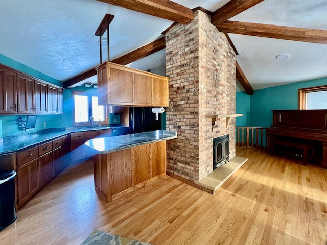 kitchen featuring kitchen peninsula, vaulted ceiling with beams, light hardwood / wood-style flooring, and a wood stove