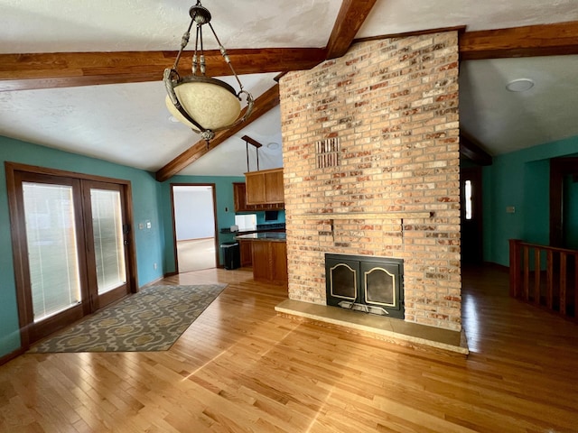 unfurnished living room featuring a fireplace, a textured ceiling, vaulted ceiling with beams, and light hardwood / wood-style floors