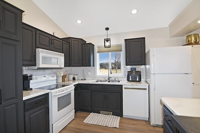 kitchen with light countertops, decorative backsplash, a sink, wood finished floors, and white appliances